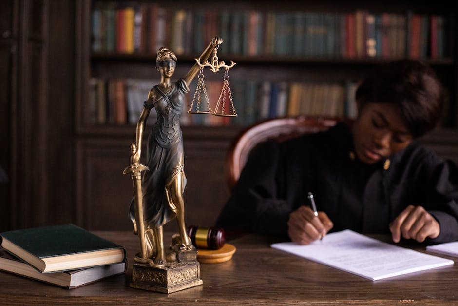 A focused judge writing on documents beside a Lady Justice statue